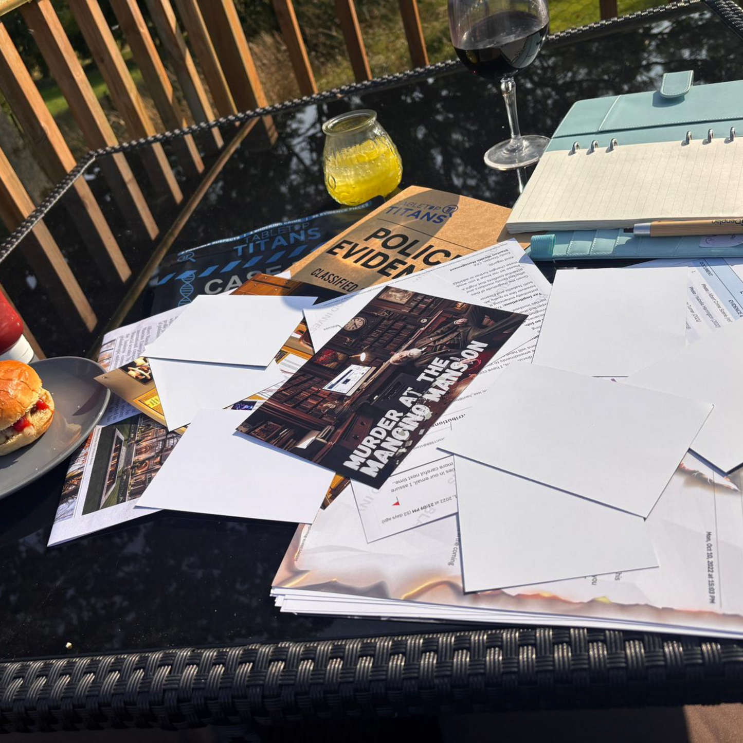 Table with papers, a book titled 'Police Evidence', a yellow candle, and a burger outdoors.